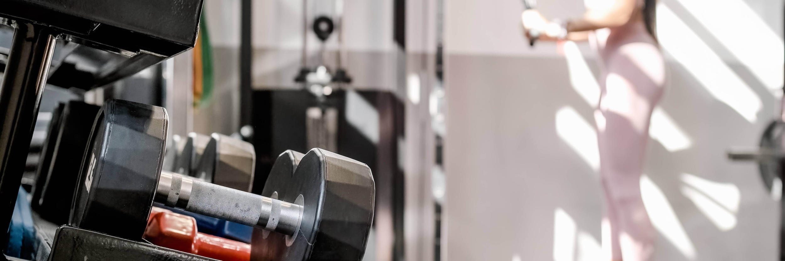 woman stretching in front of dumbbell rack