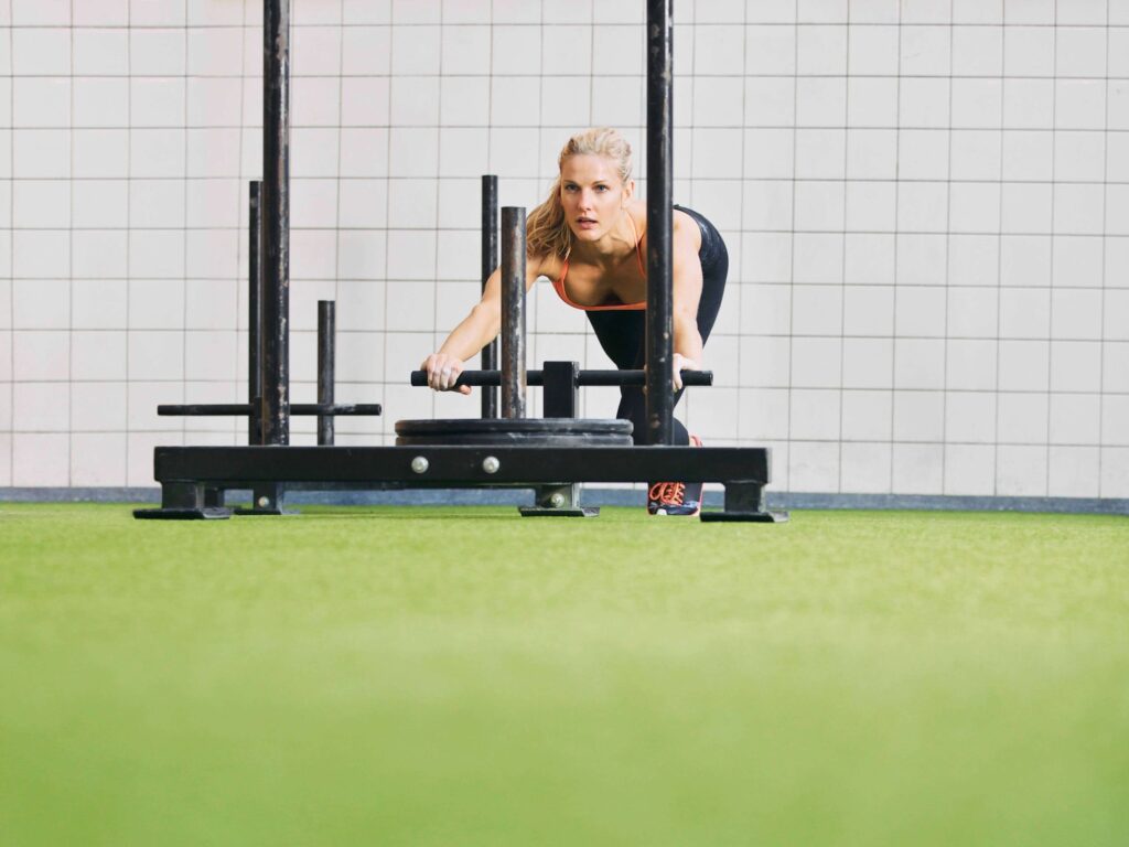 Woman pushing weighted sled across turf